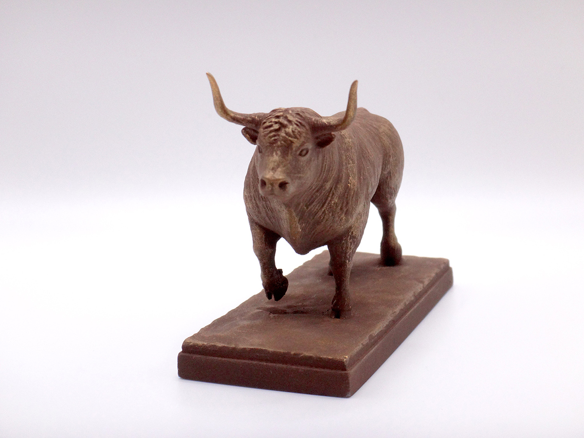 Small bull sculpture with bronze-toned surface and compact grounded form