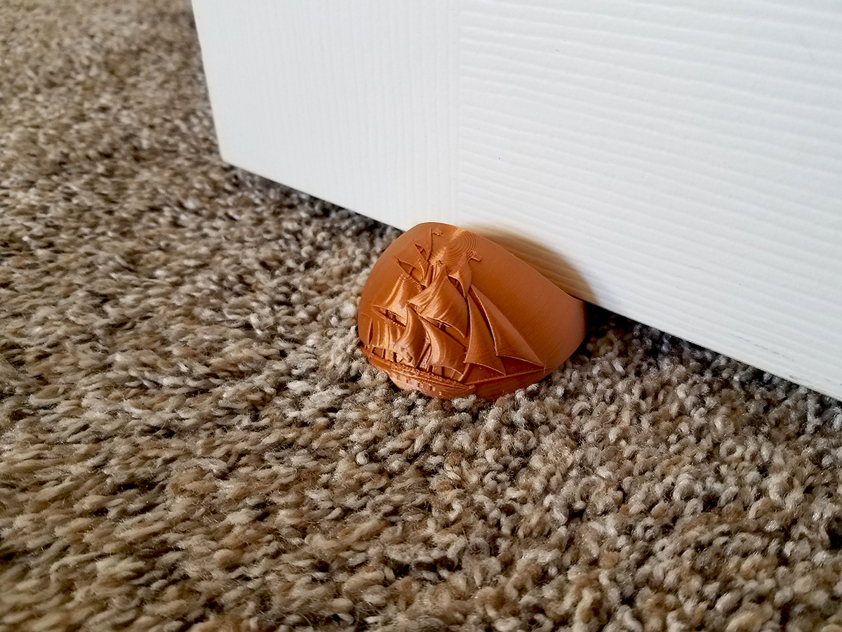 Physical version of the sailing ship door stopper securing a door on carpet flooring inside a residential interior.