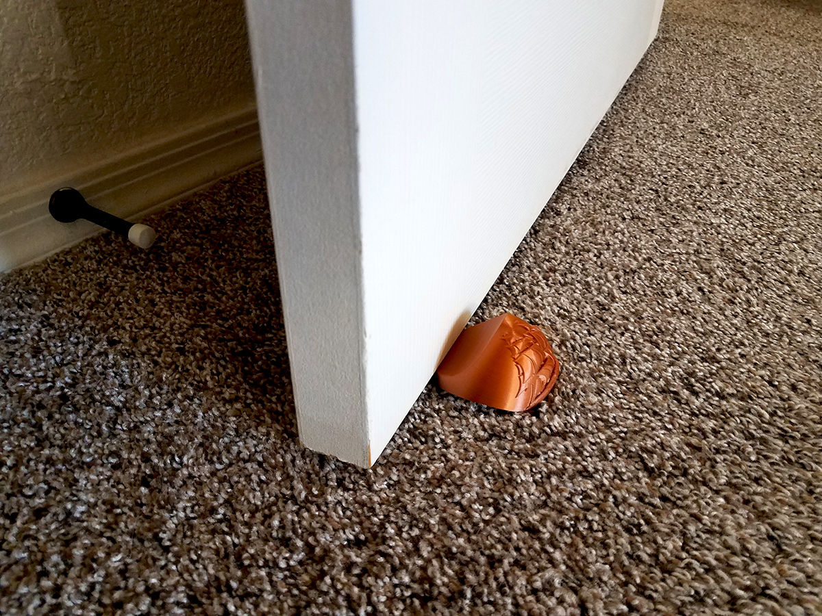 Decorative portable carpet door stopper in practical use, helping prevent accidental door closing caused by drafts or air movement.