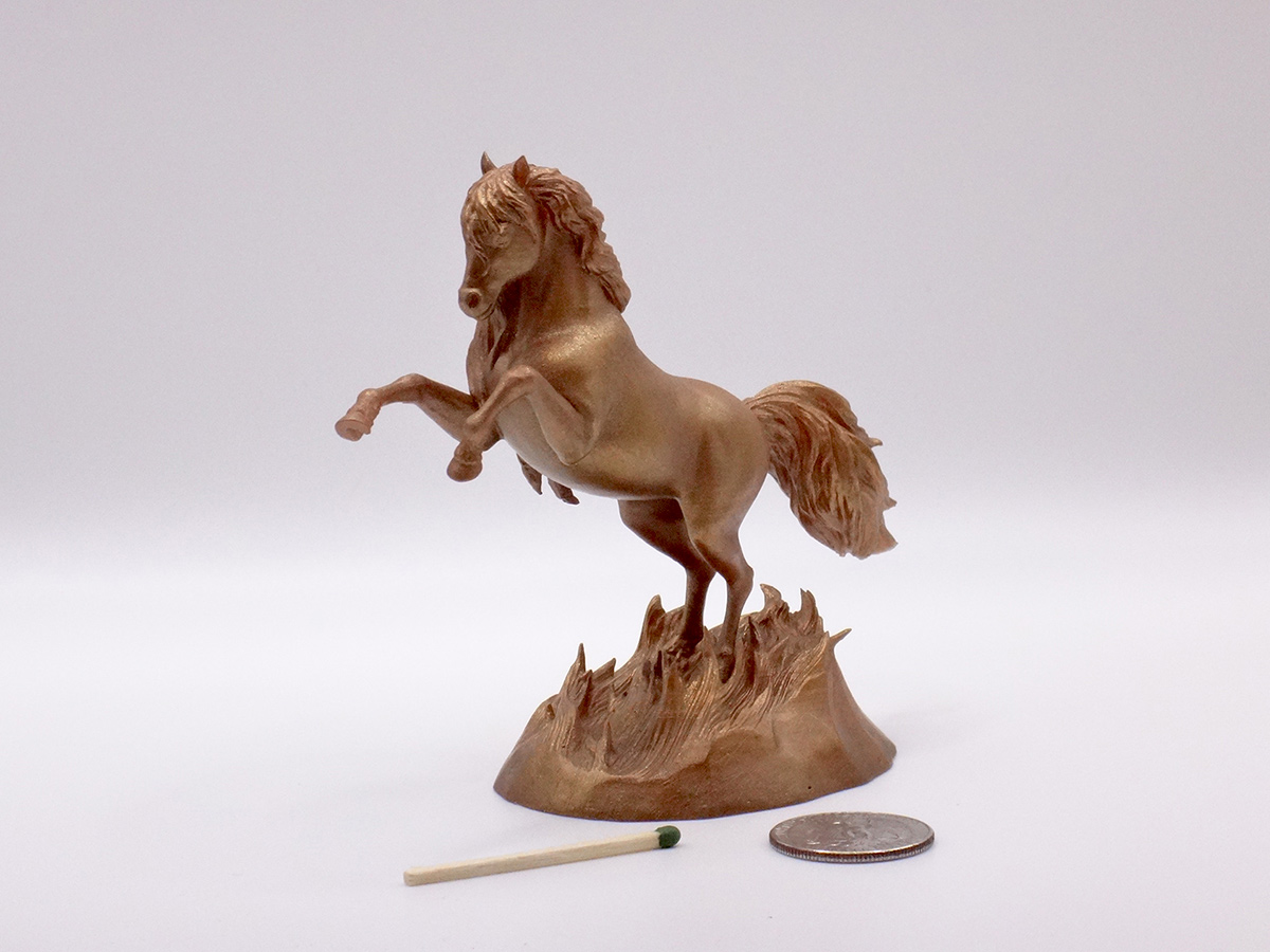 Small rearing horse sculpture with bronze-toned surface shown next to a coin and matchstick for scale