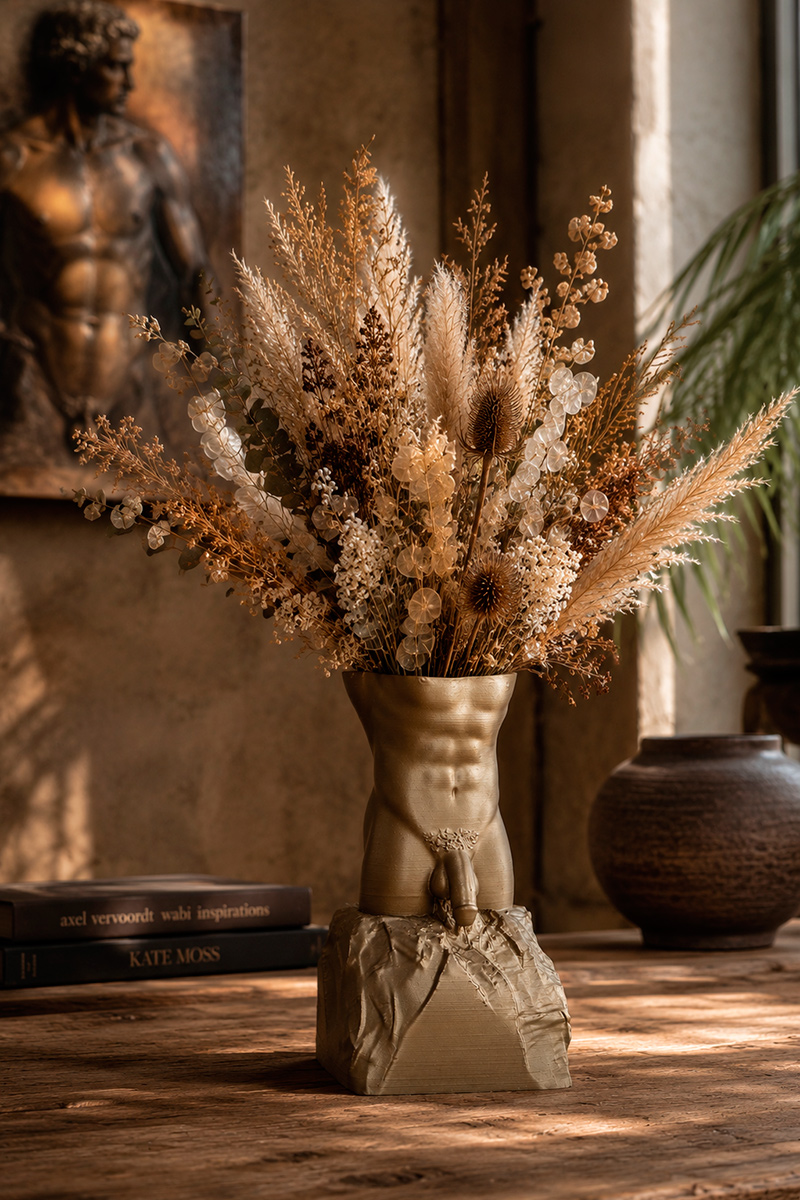 Bronze male torso sculptural vase with dried flowers displayed in a warm contemporary interior, combining figurative sculpture with functional vase design.