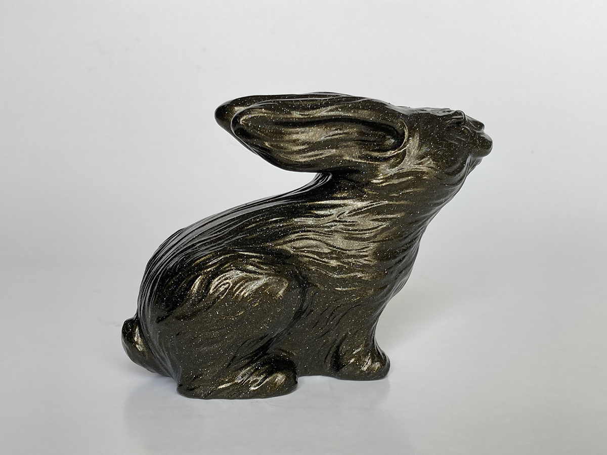 Rabbit sculpture with black and gold reflective finish, flowing surface catching light, expressive contemporary art object