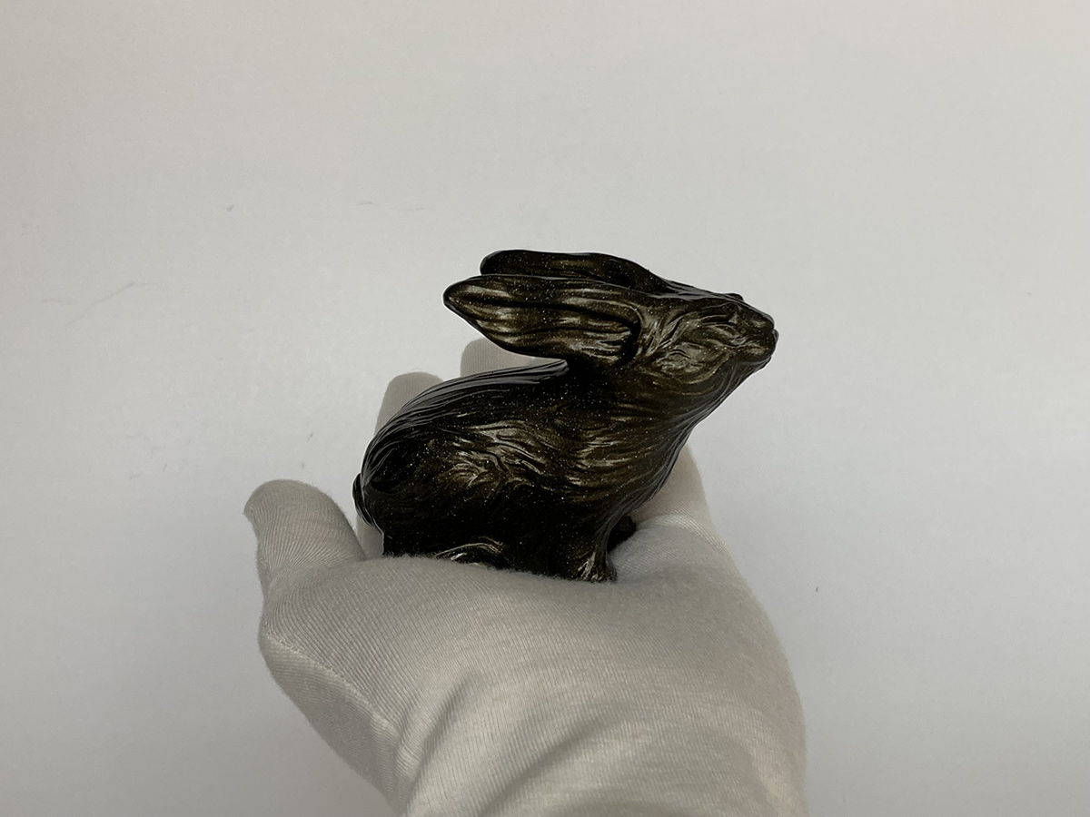Small rabbit sculpture held in hand, black and gold finish with subtle reflections, emphasizing scale and crafted detail