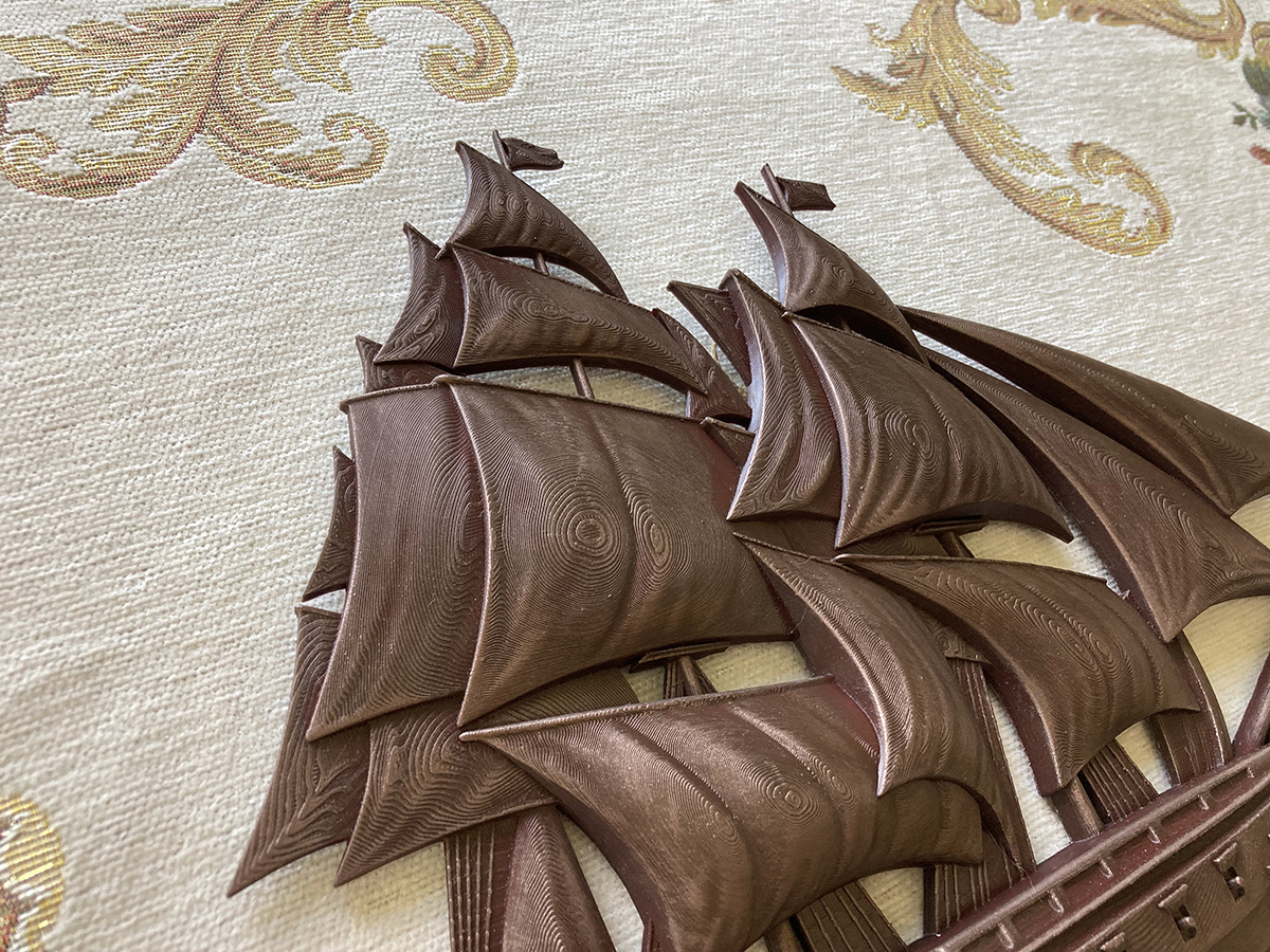 Close-up of sailing ship bas-relief sculpture showing layered surface texture and light interaction across sculpted sails