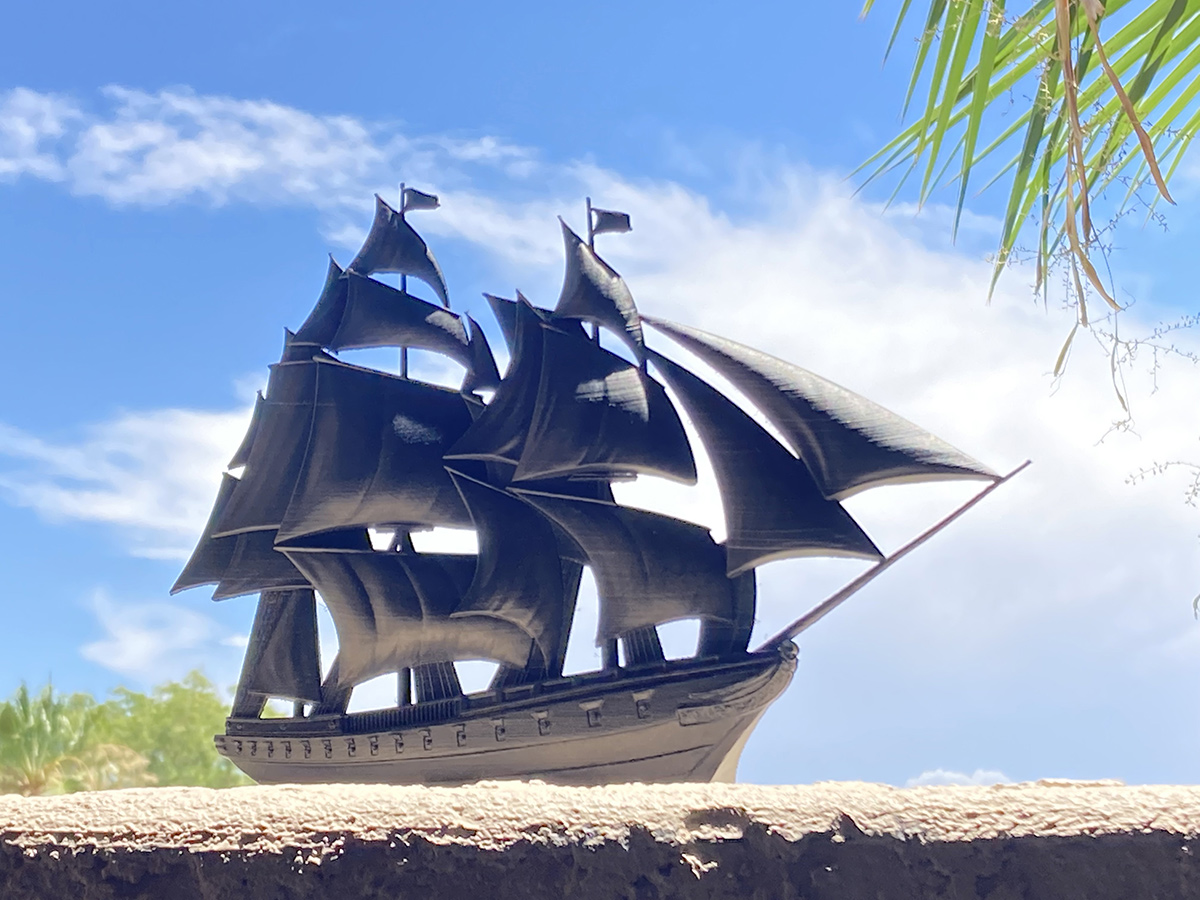 Black sailing ship sculpture silhouetted against blue sky, emphasizing shape, sails, and graphic composition
