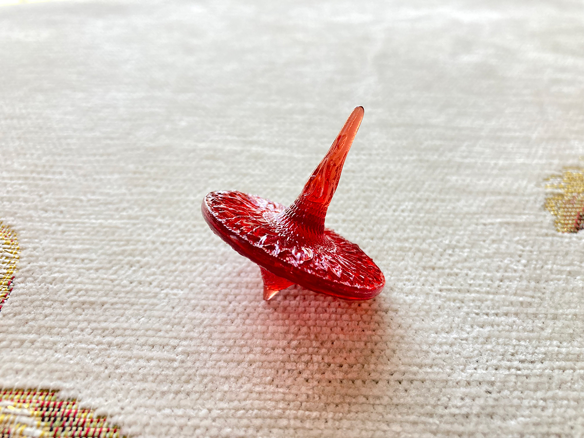 Sunflower sculptural spinning top in red transparent resin — light passing through form revealing internal structure