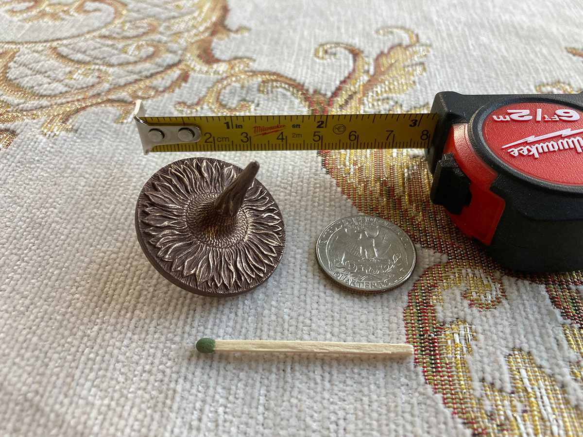 Small sunflower sculptural top with measuring tape and coin — scale reference of detailed bronze-finish object